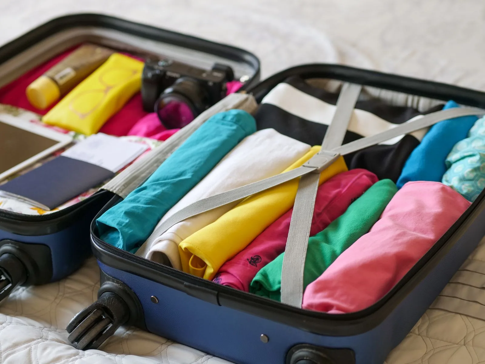 Open suitcase packed with folded colorful clothes, ready for a trip with a travel steamer
